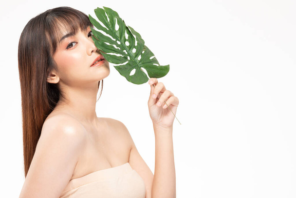 Beauty asian woman  brown hair looking smile in camera happiness and holds a large green tropical leaf in hands and covers a part of her face and cheerful with make up brush,Beauty Concept. - Photo, Image