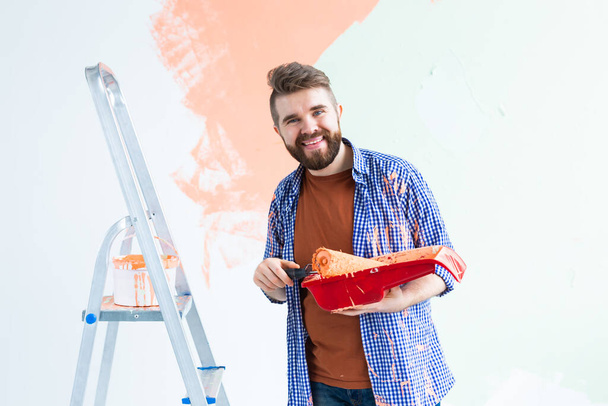 Hombre feliz pintando la pared interior del hogar. Concepto de renovación, reparación y redecoración
. - Foto, imagen