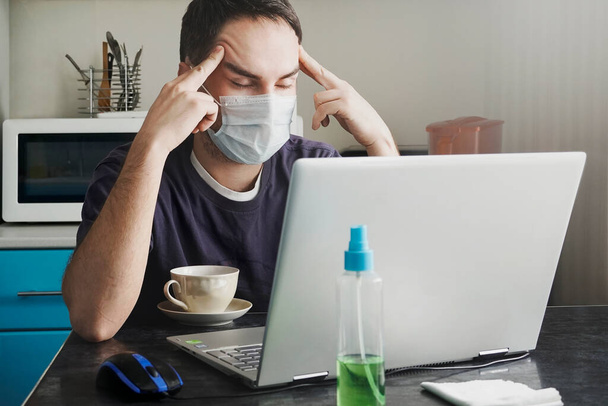 Egy fáradt, orvosi maszkban dolgozó fiatal munkás otthonról dolgozik kora reggel. Otthon maradni a világjárvány vagy a kovid 19 koronavírus járvány idején. - Fotó, kép