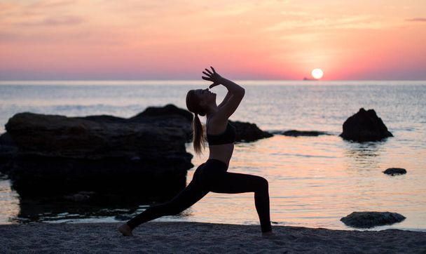 dívka má jógu praxi na pláži mezi velkými kameny. skály v moři. čas východu slunce - Fotografie, Obrázek