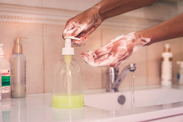 Händewaschen mit Seife unter fließendem Wasser. Eine afroamerikanische Frau wäscht sich die Hände. Druck auf die Flasche mit Seife und Wasser. - Foto, Bild