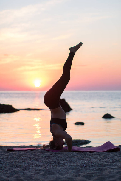 dziewczyna ma praktykę jogi na plaży wśród dużych kamieni. skały w morzu. czas wschodu słońca - Zdjęcie, obraz