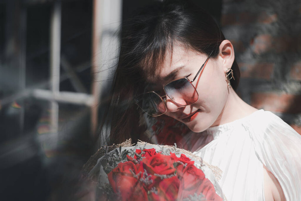 Usmívající se dívka s kyticí rudých růží, Portrét spokojené mladé ženy oblečené v bílých šatech držící kytici růží - Fotografie, Obrázek