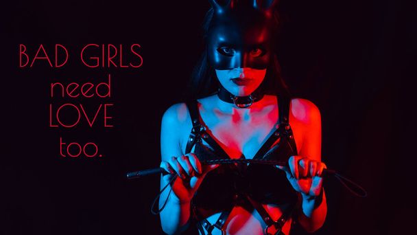 girl in a BDSM costume and a hare mask with a whip on a black background - Photo, Image