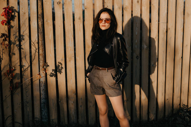 стильная юная брюнетка в кожаной куртке и шорты в модных солнцезащитных очках
 - Фото, изображение