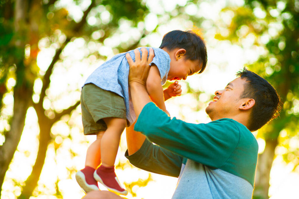 Portret van een gelukkige vader die de hand van een baby vasthoudt in het zonlicht van het stadspark. Leuke jongen met papa spelen buiten. - Foto, afbeelding