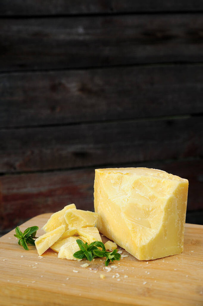 Sert parmesan peyniri, nane filizi ile süslenmiş parçalara ayrılır. Karanlık bir tahtanın üzerinde yatıyor. - Fotoğraf, Görsel
