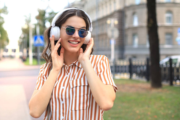 Smiling happy young beautiful woman in earphones walking outdoors in city - Fotó, kép
