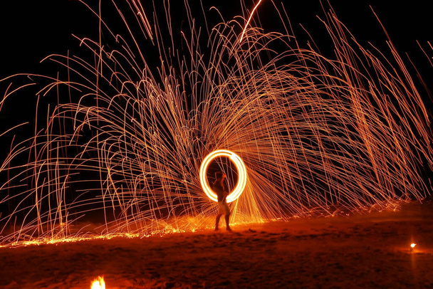 Mężczyzna pokazuje huśtawkę ognia tańczącego nocą na plaży. - Zdjęcie, obraz