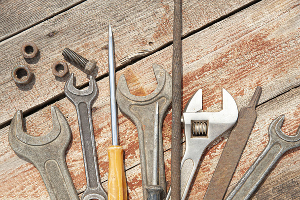 um conjunto de ferramentas manuais velhas, enferrujadas feitas com metal. Em placas de madeira são várias formas chaves, chave de fenda, arquivo, parafusos, porcas, chave ajustável forjada
 - Foto, Imagem