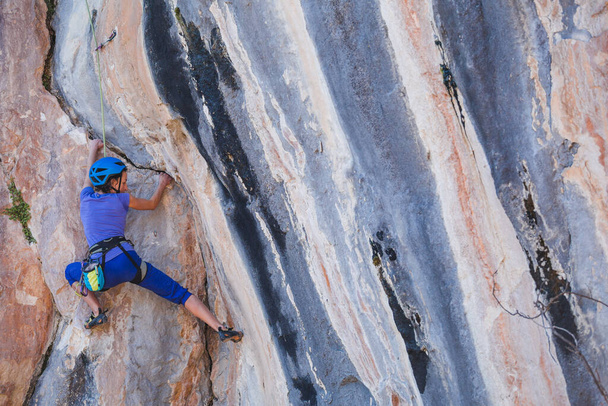 Une femme portant un casque grimpe un beau rocher bleu. Équipement de protection d'escalade. Sécurité en escalade. L'alpiniste surmonte une route difficile sur un terrain naturel. Escalade en Turquie. - Photo, image