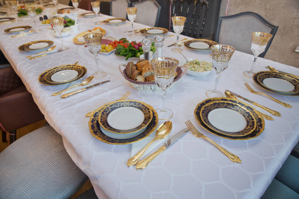 Prachtig versierde tafel met gouden borden, linnen servet, lepel, vork. Lege plaat, gouden set op houten witte tafel . - Foto, afbeelding