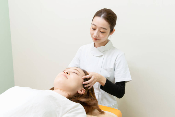 Asiatin massiert Kopf und Gesicht einer Patientin - Foto, Bild