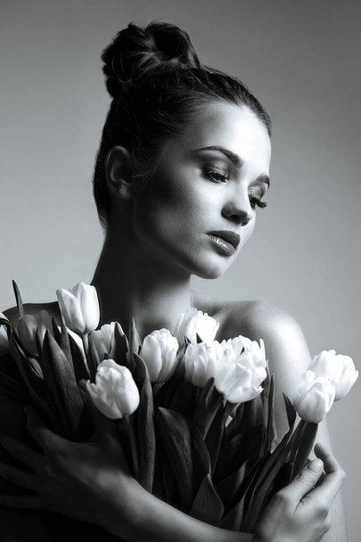 Fashion portrait of elegant young woman holding a bouquet of a white tulips. Black and white toning - Foto, Imagem