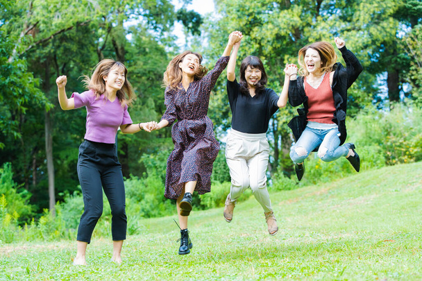 Vier junge asiatische Frauen springen lächelnd im Park - Foto, Bild