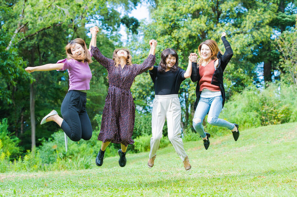 Чотири азіатські молоді жінки стрибають з посмішкою в парку. - Фото, зображення