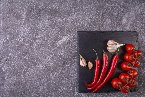 cherry tomatoes on a twig, garlic, red chilli pods on a slate stone over the top - Fotoğraf, Görsel