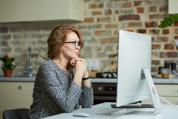 A pretty woman in glasses works remotely on a desktop computer in her studio. A female boss sits arms crossed at a video conference at home. A female student listening to an online lecture. - Photo, Image
