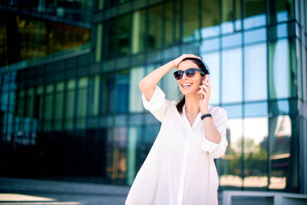 Shot of attractive happy woman talking with somebody on her mobile phone while standing outside.  - 写真・画像