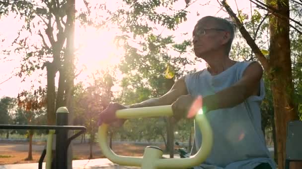 Asijský senior muž ve sportovním oblečení cvičení pro dobré zdraví na venkovní fitness vybavení ve veřejném parku za slunečného dne. zdravý životní styl koncept. - Záběry, video