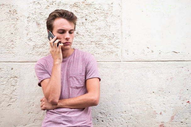 Портрет красивый молодой человек разговаривает с мобильным телефоном, прислонившись к стене
 - Фото, изображение
