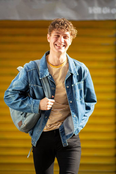 Portrait happy young man with bag walking by yellow background  - Φωτογραφία, εικόνα