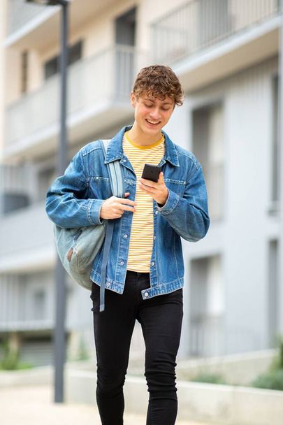 πορτρέτο νεαρός άνδρας με τα πόδια με τσάντα και κινητό τηλέφωνο έξω - Φωτογραφία, εικόνα