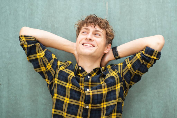 Portret szczęśliwy człowiek opierający się o zieloną ścianę z rękami za głową - Zdjęcie, obraz