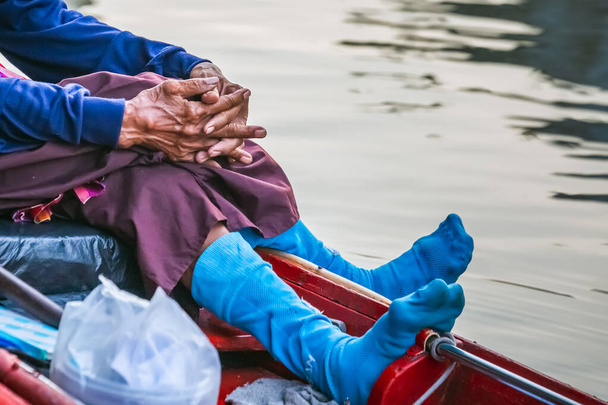 伝統的なボートを漕いでいる有名なパタヤ・フローティングマーケットのボートに乗っている老人の青い靴下。村人たちは伝統的な食べ物やお土産を売る. - 写真・画像