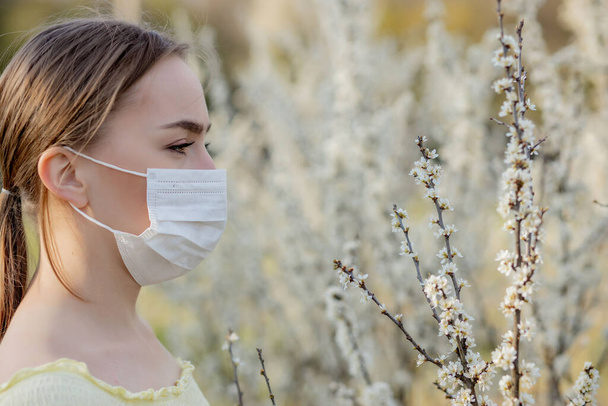 Girl in a medical mask. Girl in the spring among the blooming garden. A girl in a protective medical mask. Spring allergy concept. - Fotografie, Obrázek