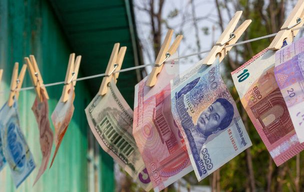 Foreign currency banknotes hanging on wooden clothespins on a rope. Laundering money. Selective focus - Foto, Imagen