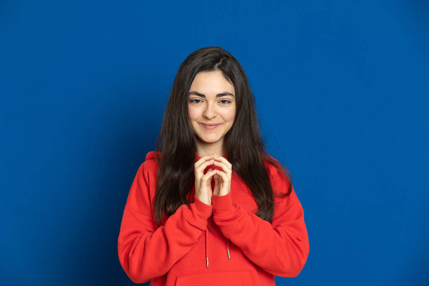 Brunette jong meisje met een rode trui op een blauwe achtergrond - Foto, afbeelding