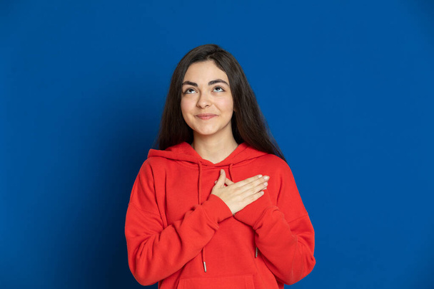 Brunette jong meisje met een rode trui op een blauwe achtergrond - Foto, afbeelding