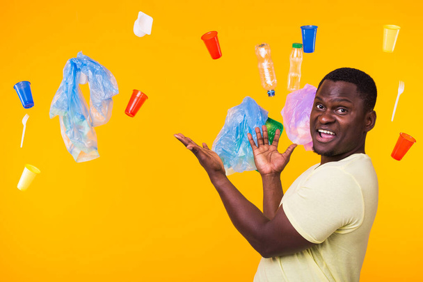 Journée mondiale de l'environnement, problème du recyclage du plastique et concept de catastrophe environnementale - Surpris homme afro-américain regardant les ordures sur fond jaune
. - Photo, image