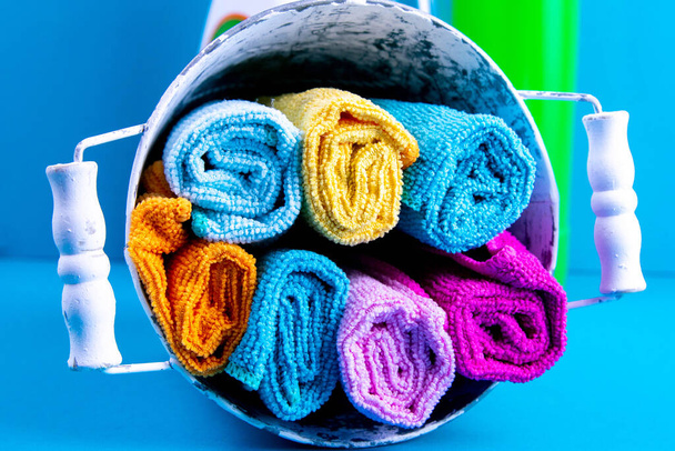 Toalhas coloridas, balde e produtos de limpeza em um fundo azul. Detergente para diferentes superfícies na cozinha, banheiro e outros quartos. Fechar.
. - Foto, Imagem
