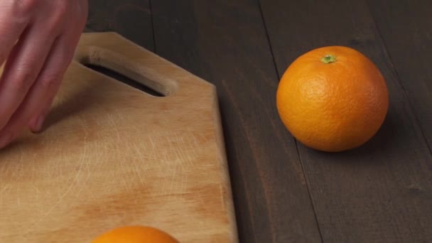 Slicing an orange on a kitchen cutting Board, wooden table as background, close view. Glass of orange juice. - Πλάνα, βίντεο