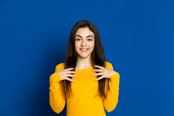 Brunette young girl wearing yellow jersey on a blue background - Photo, image