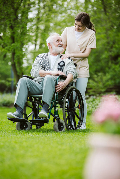 Senior man on the wheelchair in the garden of professional nursing home - Foto, afbeelding