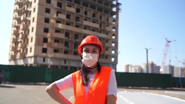Portrait of female construction worker in medical mask and overalls on background of house under construction. - Video