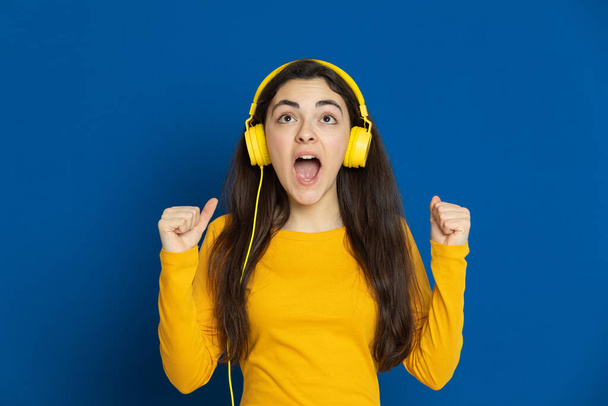 Brunette young girl wearing yellow jersey on a blue background - Fotó, kép
