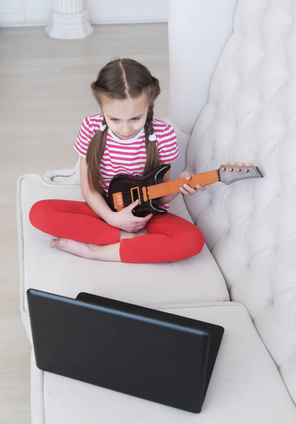  Clases en línea. Chica aprende a tocar la guitarra en casa con el ordenador portátil. Concepto de educación en casa
. - Foto, imagen