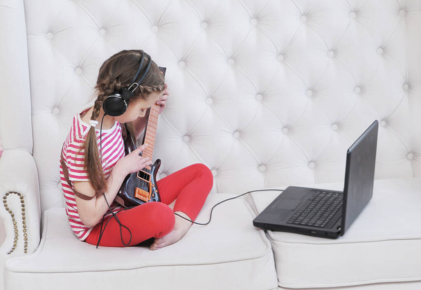  Clases en línea. Chica aprende a tocar la guitarra en casa con el ordenador portátil. Concepto de educación en casa
. - Foto, imagen