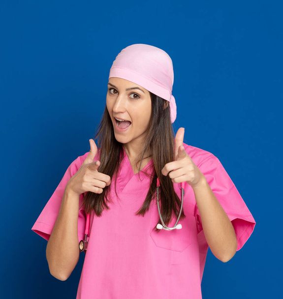 Fiatal orvos rózsaszín egyenruhában, kék háttérrel - Fotó, kép