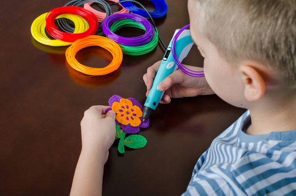 Chłopiec używający długopisu 3D. Szczęśliwe dziecko robi kwiat z kolorowego tworzywa ABS. Kreatywne hobby w domu, technologia, wypoczynek, koncepcja edukacji. - Zdjęcie, obraz