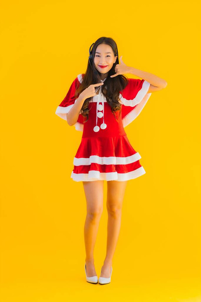 Portret piękna młoda azjatycka kobieta nosić ubrania Boże Narodzenie i kapelusz ze słuchawką lub słuchawki dla call center na żółtym odizolowanym tle - Zdjęcie, obraz