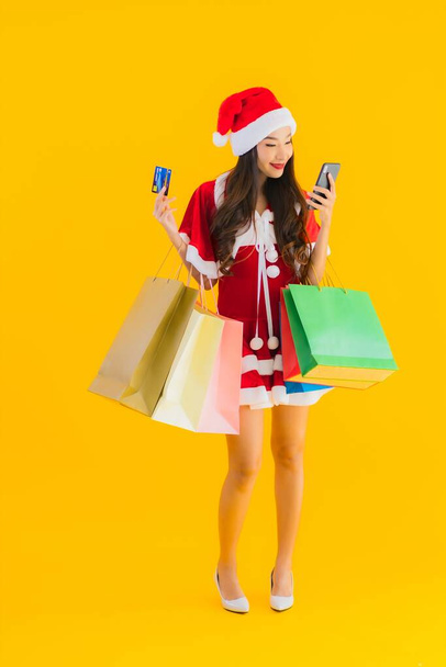 Portrait beautiful young asian woman wear christmas clothes hat with a lot of shopping bag on yellow isolated background - Foto, imagen