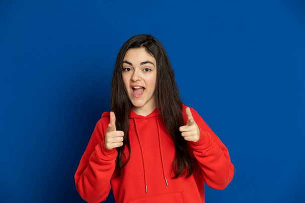 Brunette jong meisje draagt rode trui op een blauwe achtergrond - Foto, afbeelding