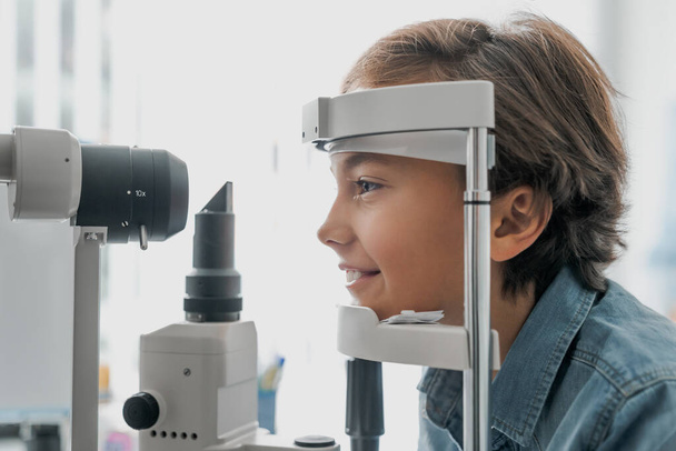 Side view shot of boy checking vision with tonometer at eye clinic - Фото, изображение