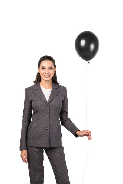 Isolated portrait of smiling young European businesswoman in elegant suit holding black balloon. Concept of celebration and success - Φωτογραφία, εικόνα