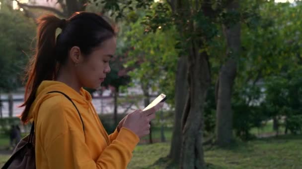 4K Happy asian woman take a walk in the park and using smartphone in Taipei. Girl smile while used phone device for surfing the internet, checks social network in beautiful Taiwan garden-Dan - Footage, Video